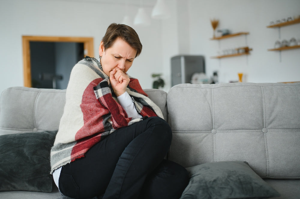 Femme congelée malade des années 50 assise sur un canapé dans un salon couvert d'éternuements chauds de plaid, le nez rassis se sent malsain, froid de saison, concept du système immunitaire affaibli